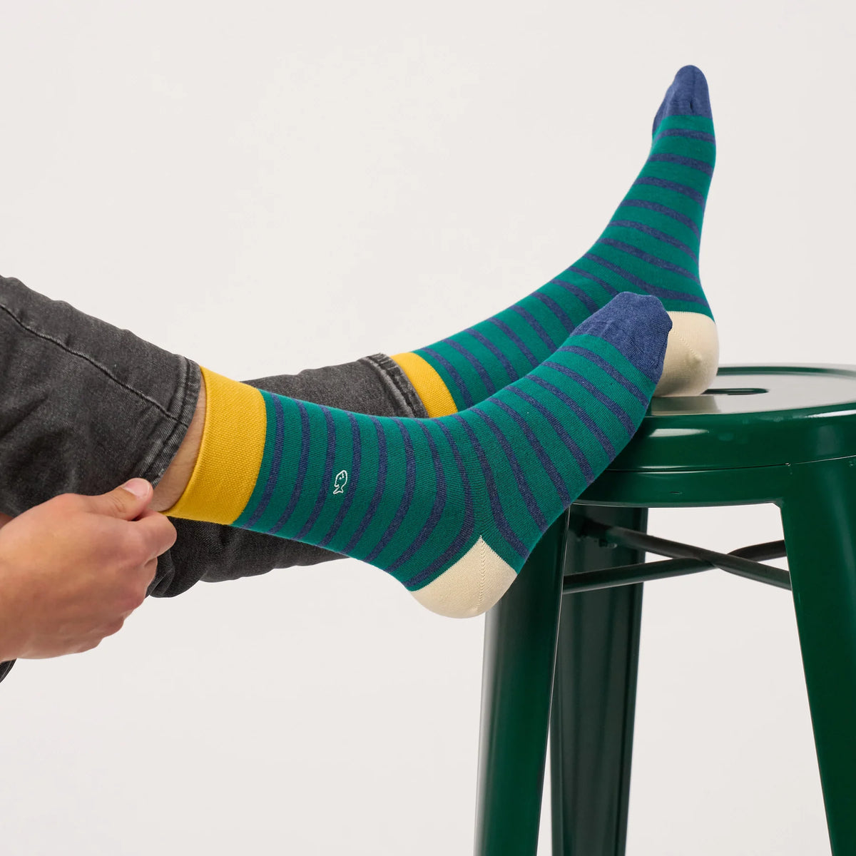 Paire de chaussettes rayures vert et bleu BillyBelt portées, pieds posés sur un tabouret vert