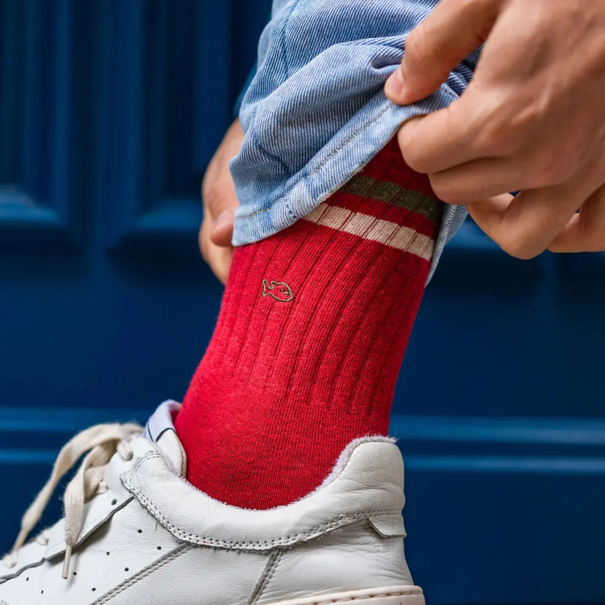 Tige rouge côtelée relevée au-dessus d'une basket blanche, poisson brodé kaki et bandes kaki et écrue.