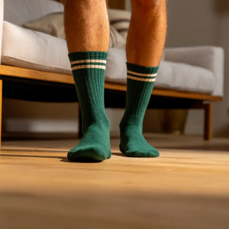 Paire côtelée vert sapin portée debout sur un parquet, double bande écrue en haut de tige bien visible.