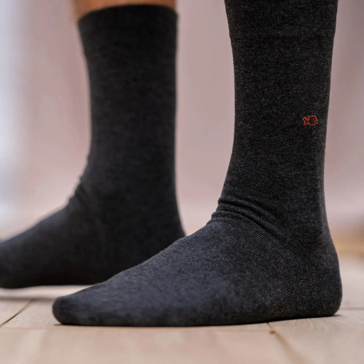 Chaussettes gris souris portées de profil sur un parquet clair, broderie poisson rouge