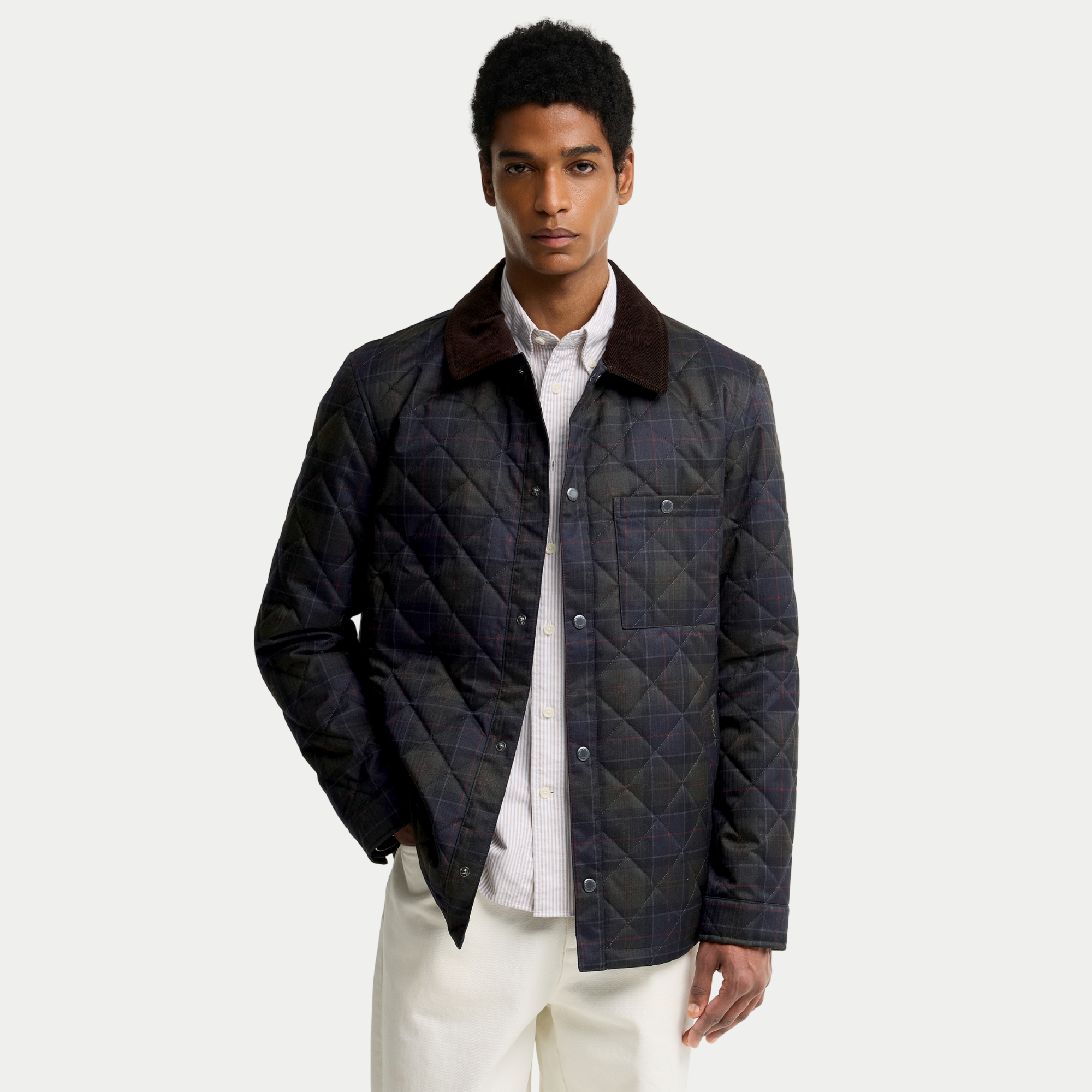Veste-chemise matelassée Barbour tartan olive foncé portée ouverte sur une chemise rayée, pressions métal sur le devant