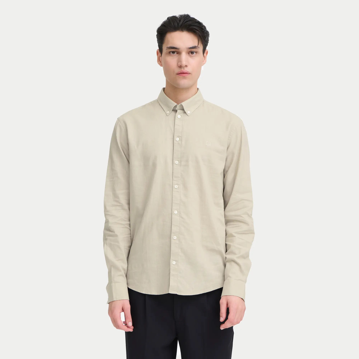 Chemise en lin naturel portée, boutonnée jusqu'en haut sur un pantalon noir