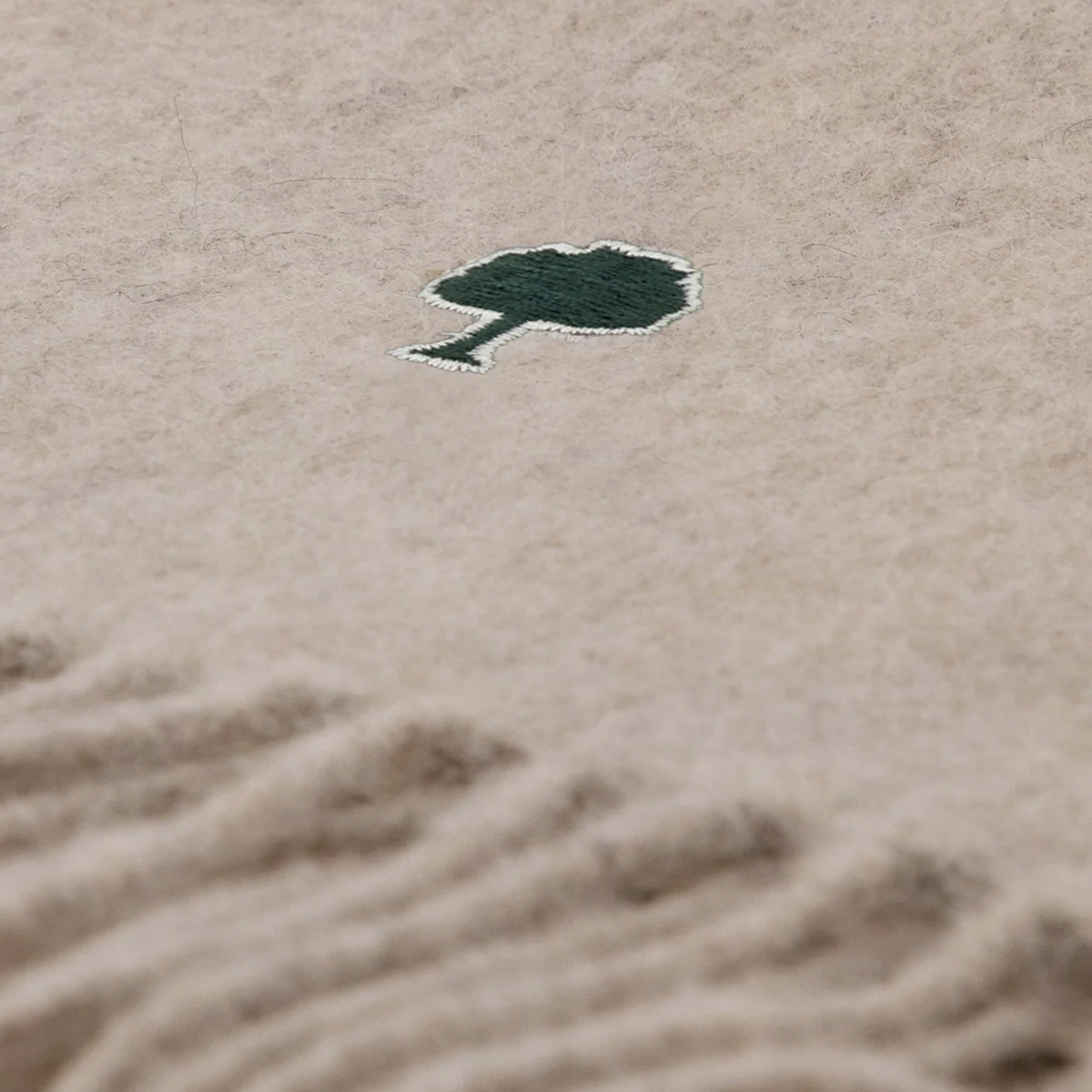 Détail de la laine beige chinée, fibres mêlées, et arbre Faguo brodé vert sapin cerclé d'écru