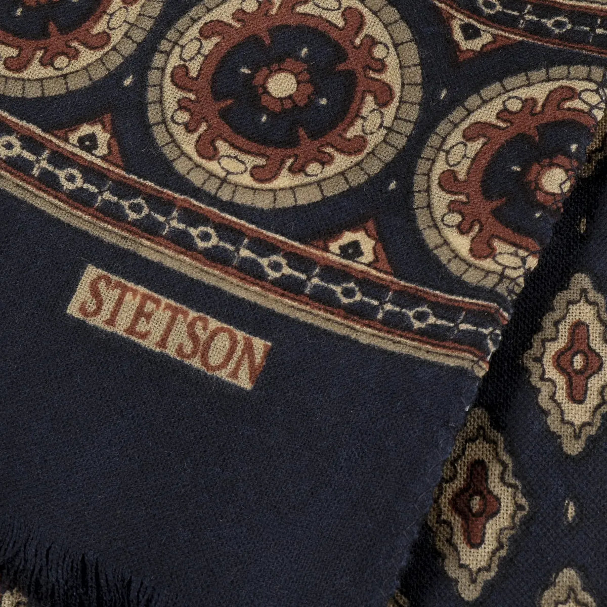 Extrémité de l’écharpe Ornamentals Stetson : bordure à médaillons rouille et beige, logo de la marque et franges