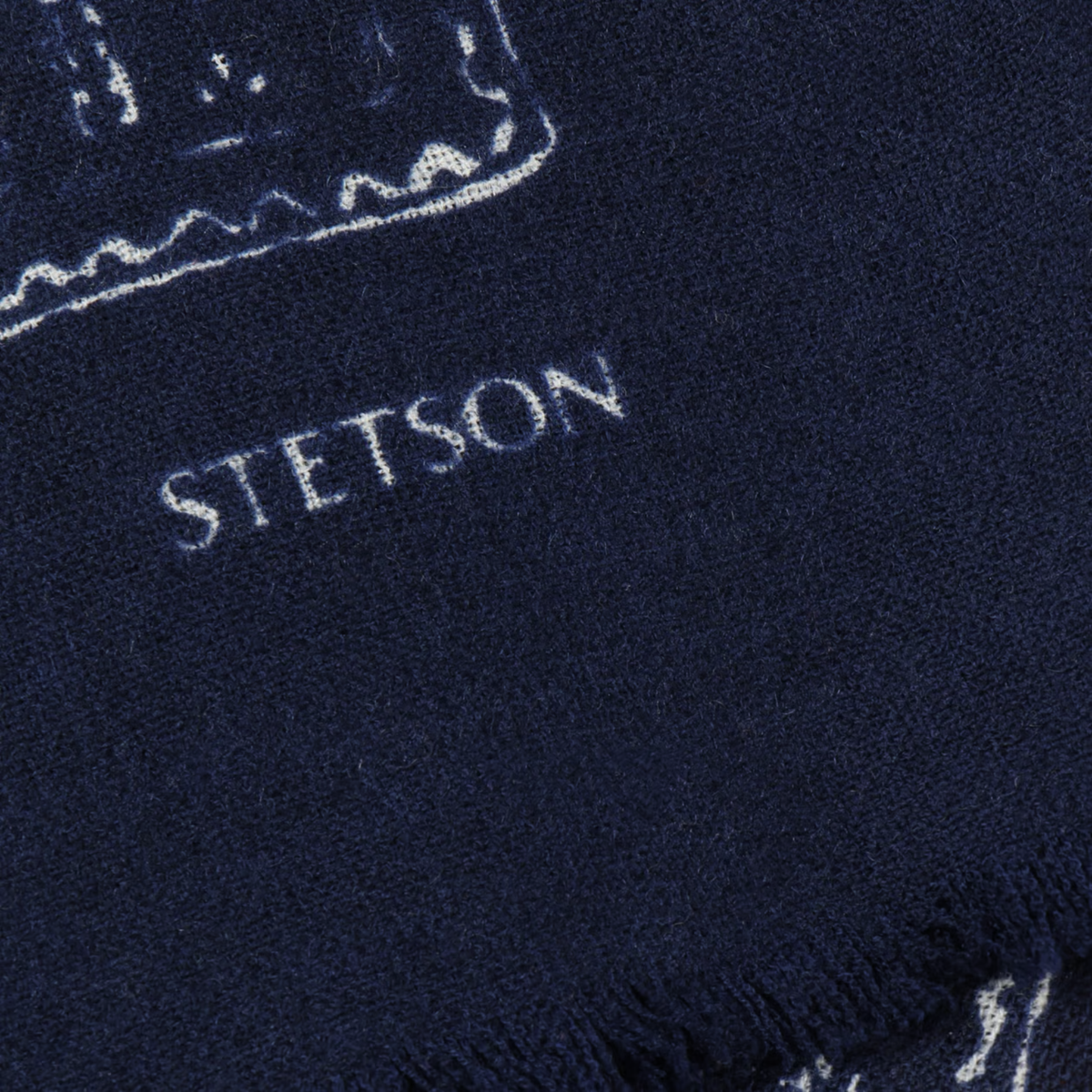 Gros plan du logo Stetson blanc sur la laine bleu marine de l'écharpe Ornaments, près des franges