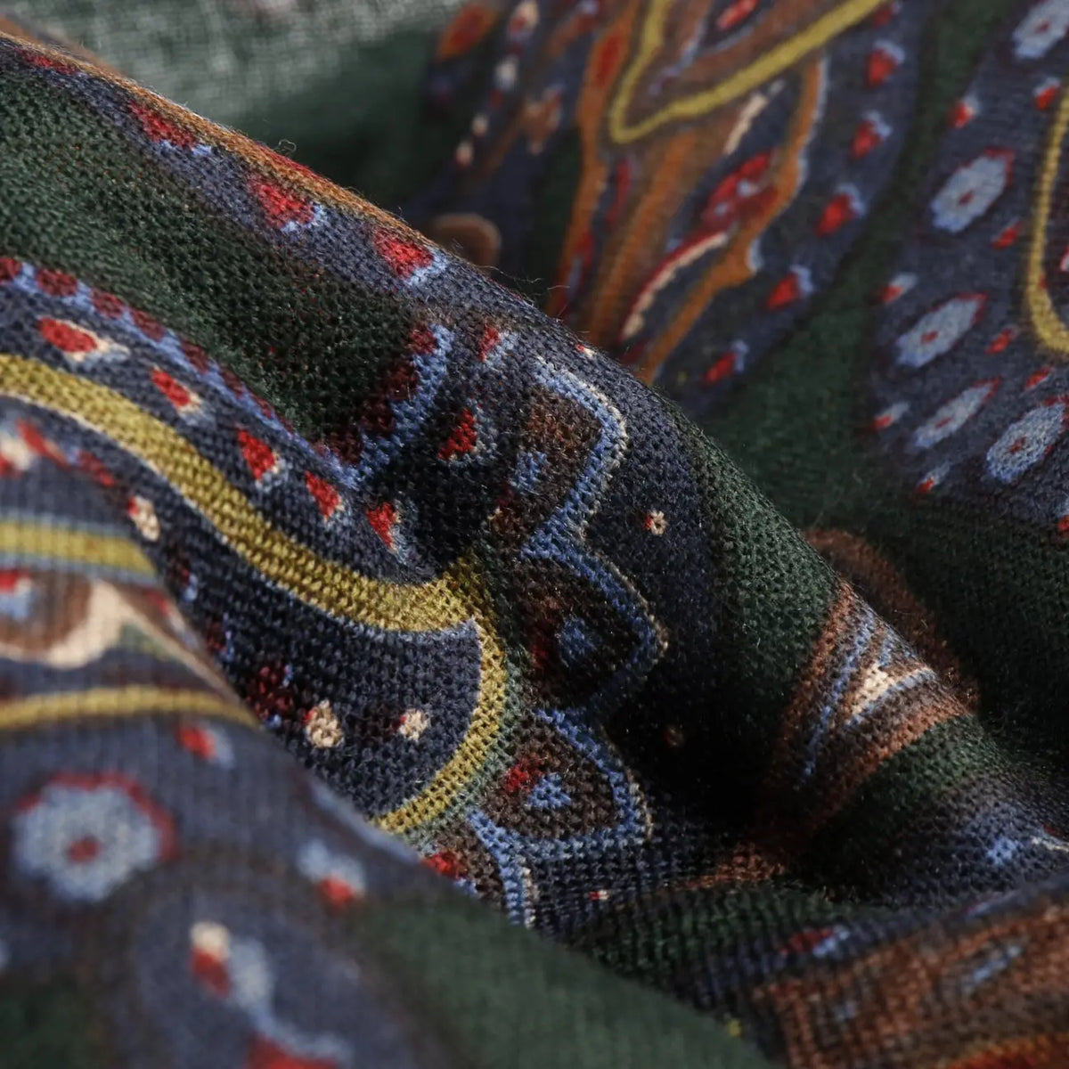 Gros plan sur la laine tissée de l'écharpe Paisley Stetson, motif rouille, moutarde et bleu sur fond vert foncé