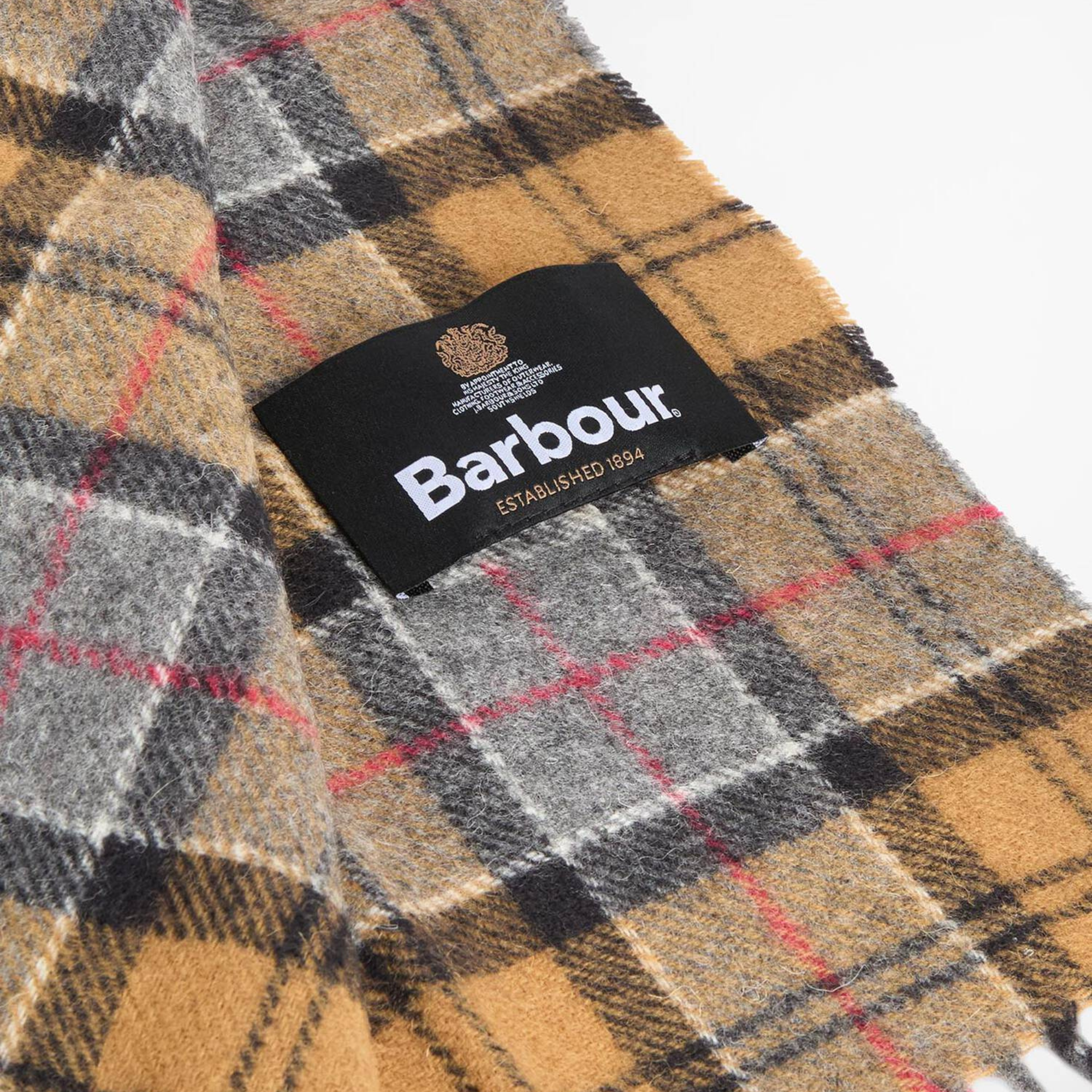 Détail de l'étiquette tissée Barbour sur l'écharpe tartan ocre moutarde, carreaux gris et noirs et fins filets rouges