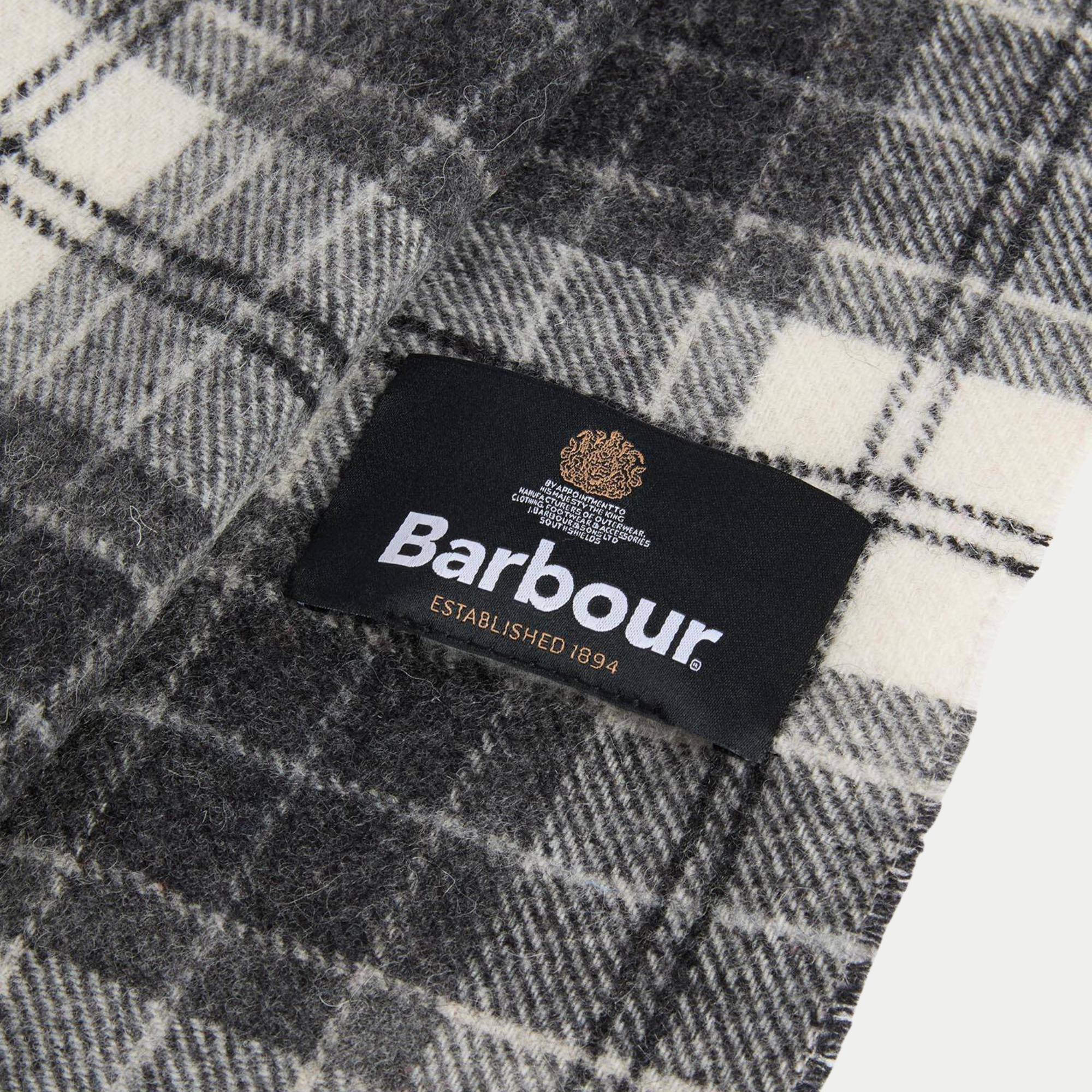Gros plan sur l'étiquette tissée Barbour et la laine à carreaux gris et écru de l'écharpe Monochrome Tartan