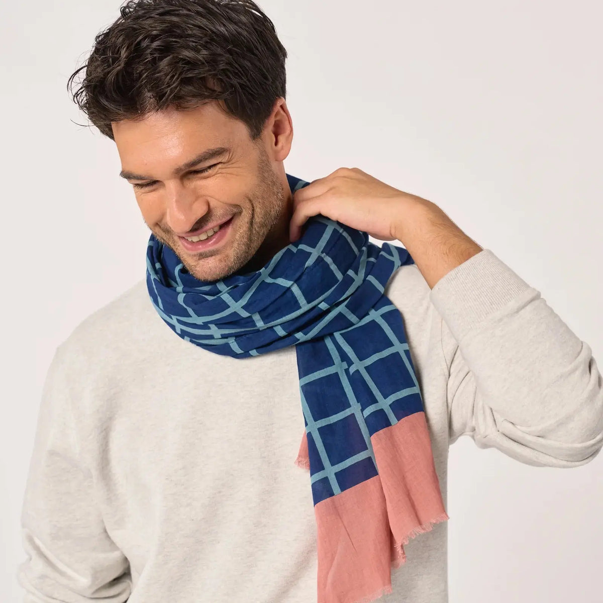 Foulard à quadrillage bleu ciel noué au cou, les deux pans rose terracotta descendant sur la poitrine