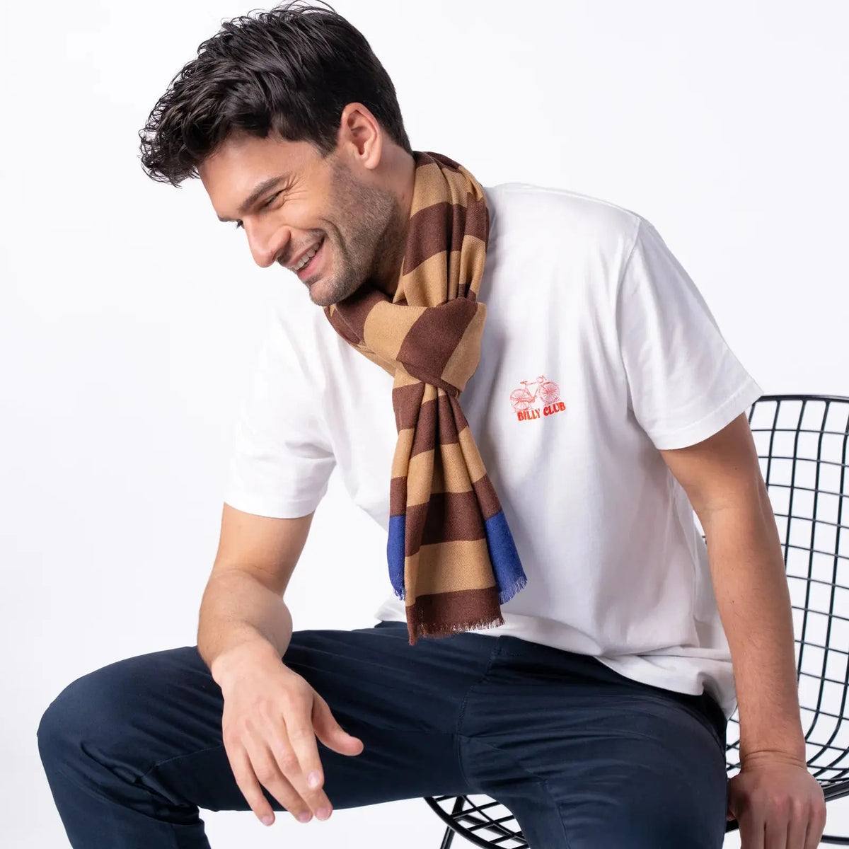 Foulard en laine rayé marron et camel noué au cou, aplat bleu roi apparaissant juste sous les franges