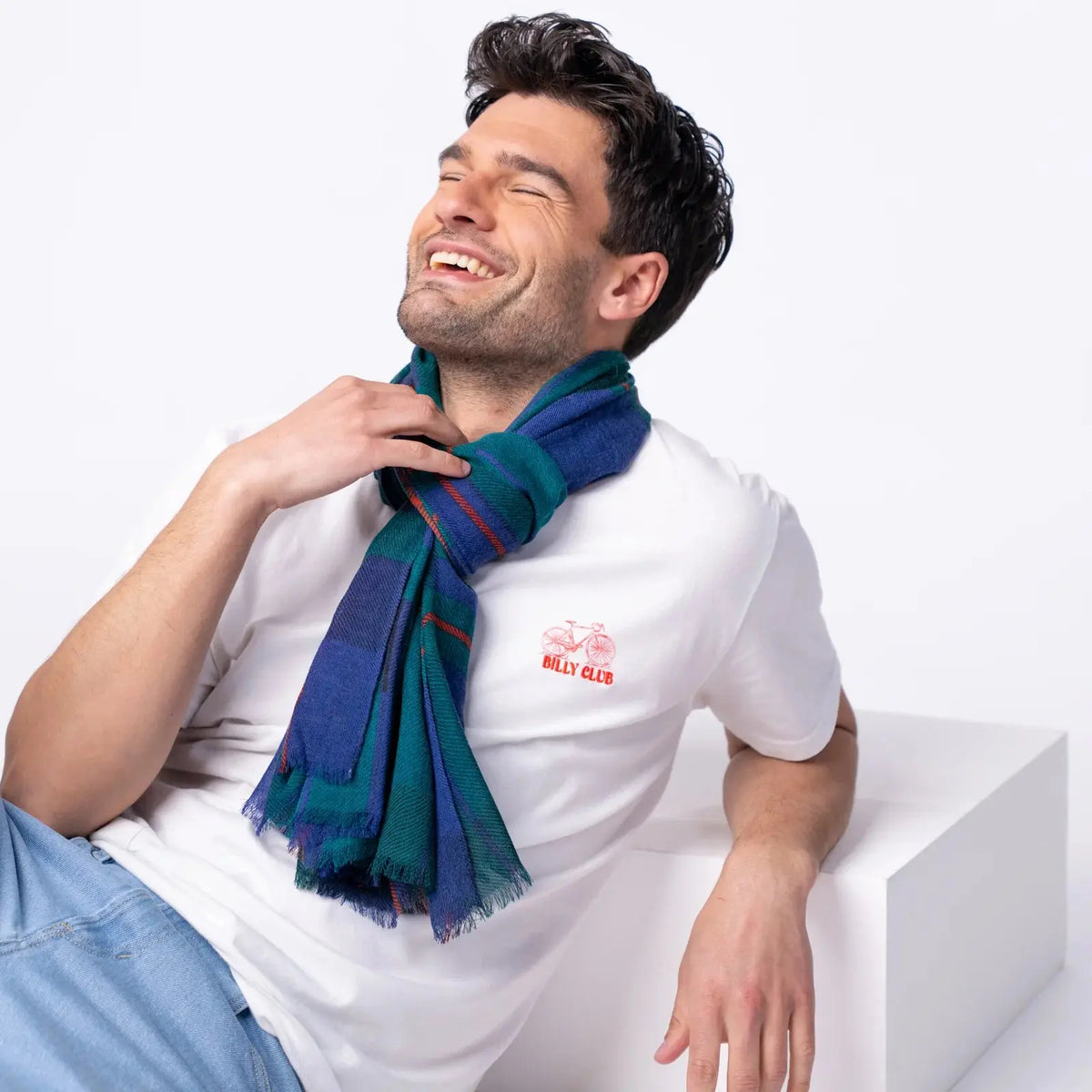 Foulard en laine à carreaux bleu roi et vert sapin noué au cou, pans frangés devant le buste
