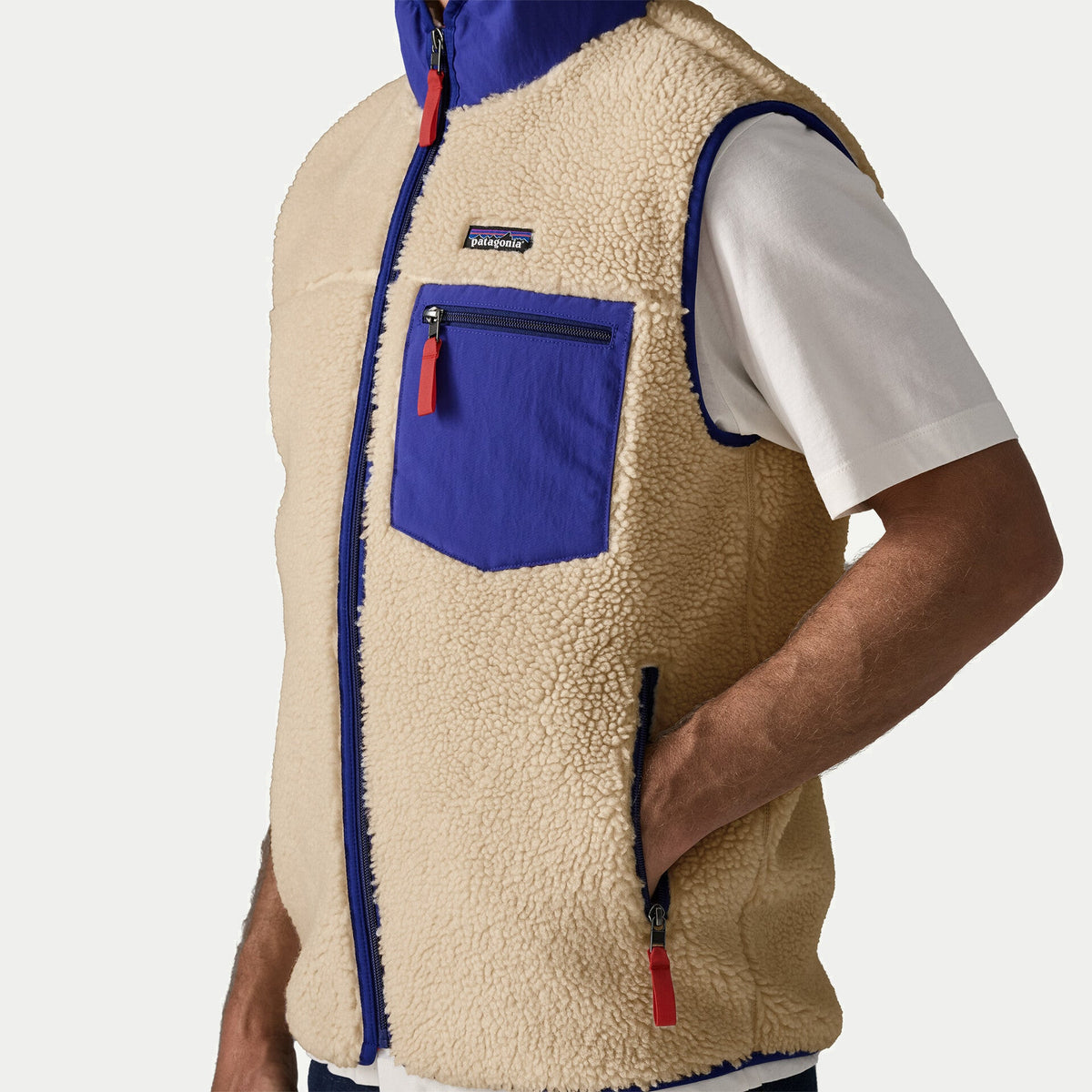 Détail buste du gilet Retro-X Patagonia : étiquette de marque, poche poitrine cobalt zippée et zip central sur sherpa écru