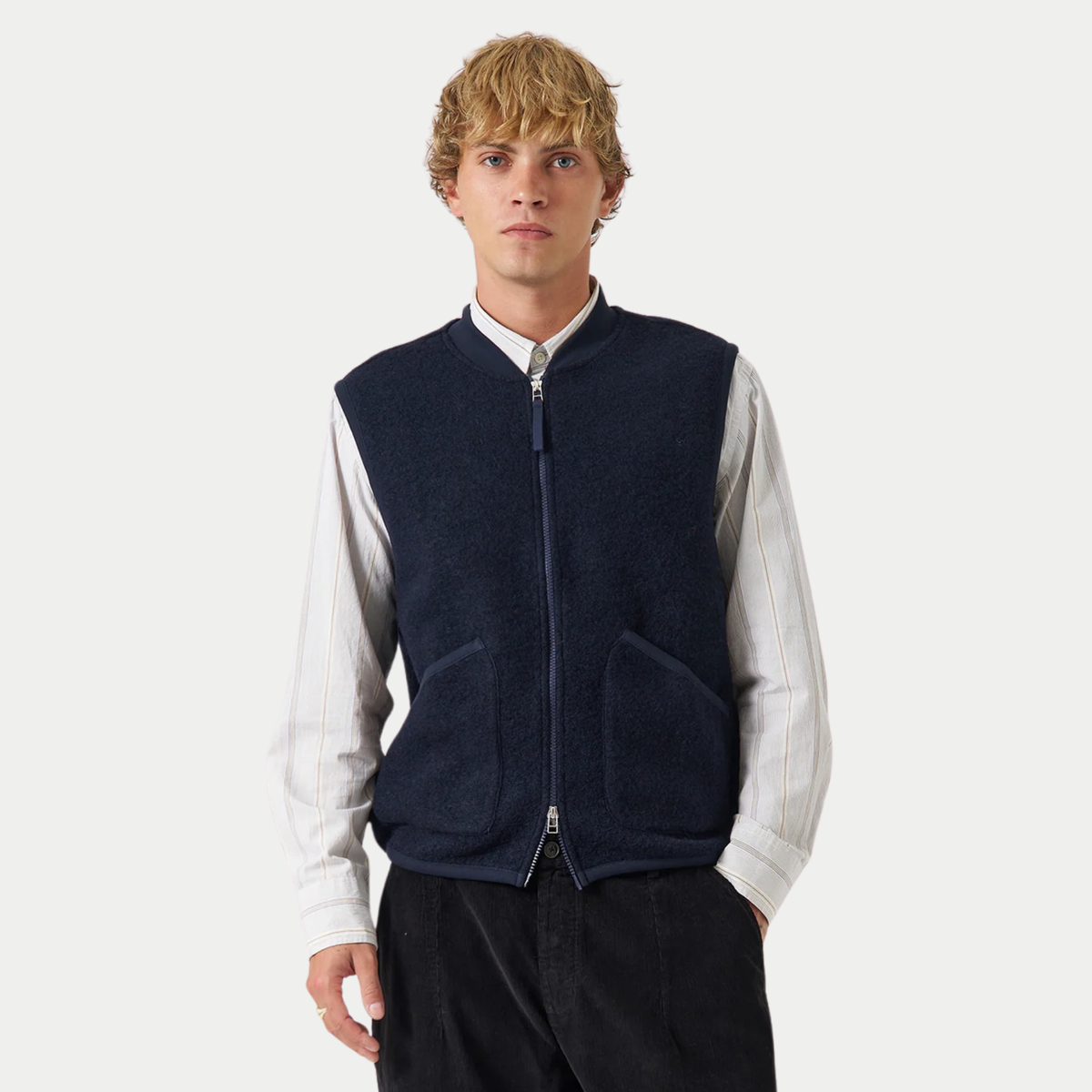 Gilet zippé Universal Works bleu marine porté fermé sur une chemise rayée, vue de face
