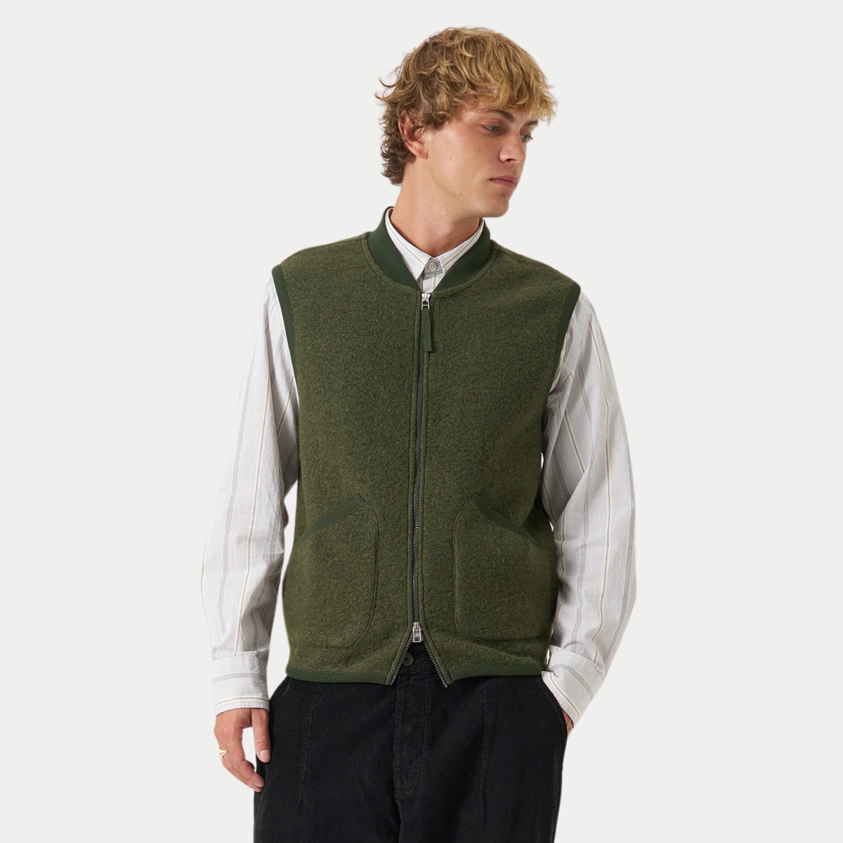 Gilet zippé Universal Works vert olive porté fermé sur une chemise rayée, vue de face