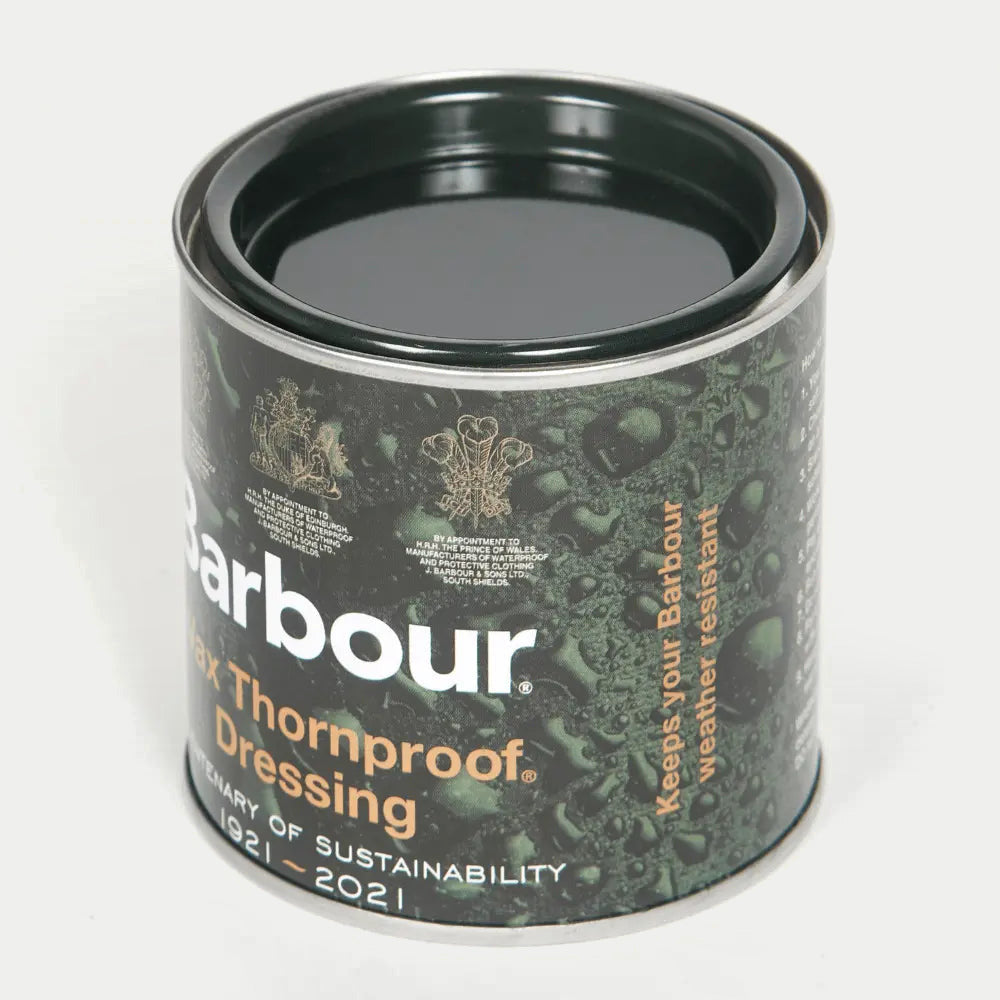 Pot de cire Barbour ouvert vu de trois quarts, la cire sombre visible sous le couvercle serti