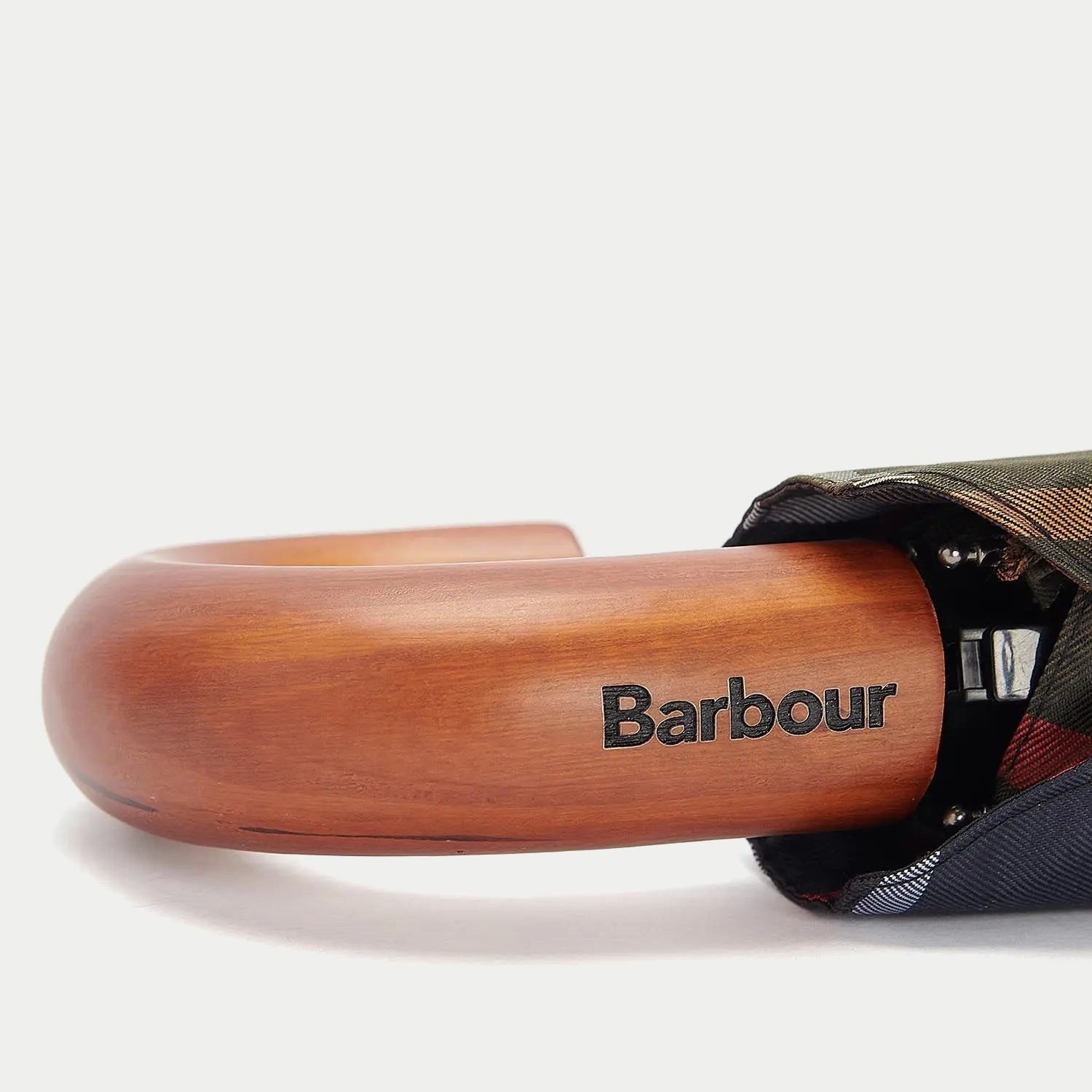 Gros plan sur la poignée courbée en bois verni du mini parapluie Barbour, logo gravé, toile pliante repliée