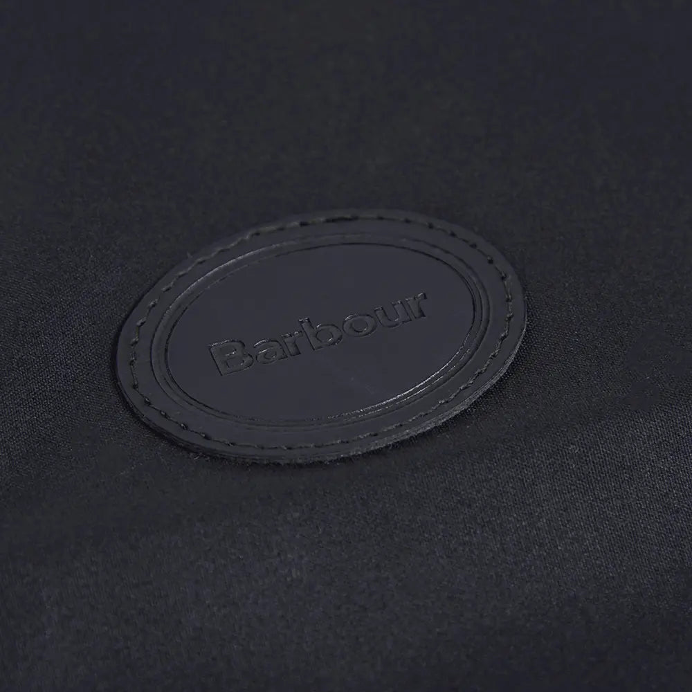 Macro du patch cuir ovale Barbour embossé sur le coton ciré noir du manteau