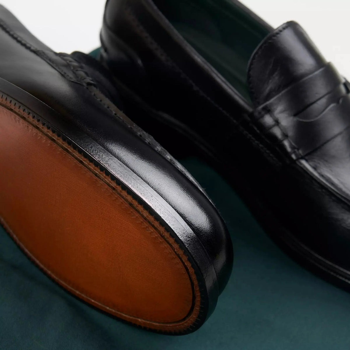 Mocassins Craft James Lo noirs en gros plan sur tissu vert, semelle cuir cognac