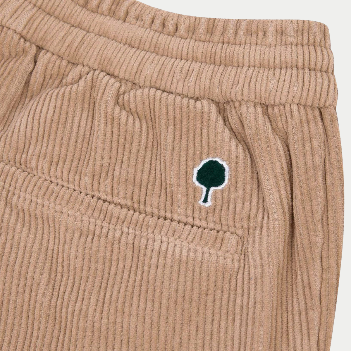 Gros plan sur les larges côtes du velours beige et le logo arbre brodé vert sapin du Pantalon Dreuille Faguo