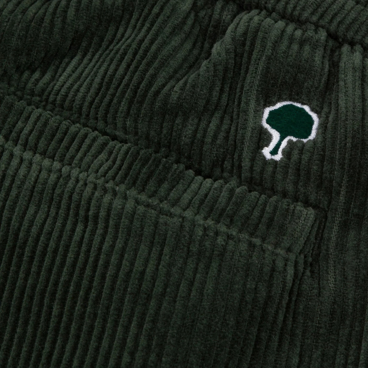 Gros plan sur les larges côtes du velours vert foncé et le logo arbre brodé blanc et vert du Pantalon Dreuille Faguo