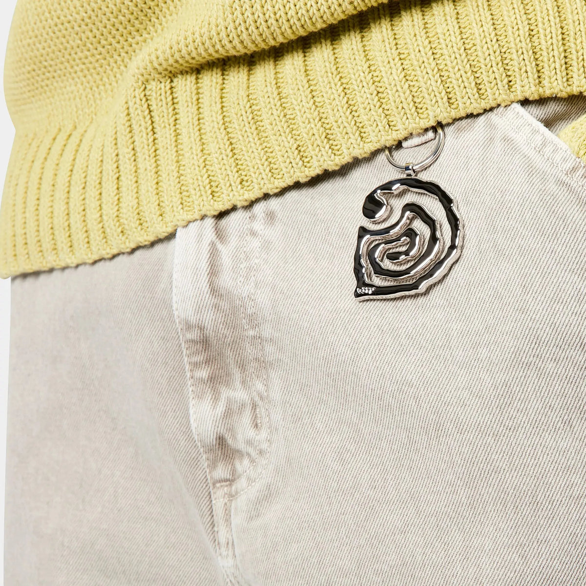 Porte-clés Helix argenté accroché au passant d'un pantalon clair, spirale pendante contre la poche