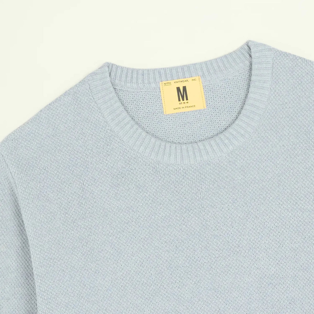 Gros plan de l'encolure du Pull Agop Light Indigo, étiquette Nitto et grain perlé de la maille coton