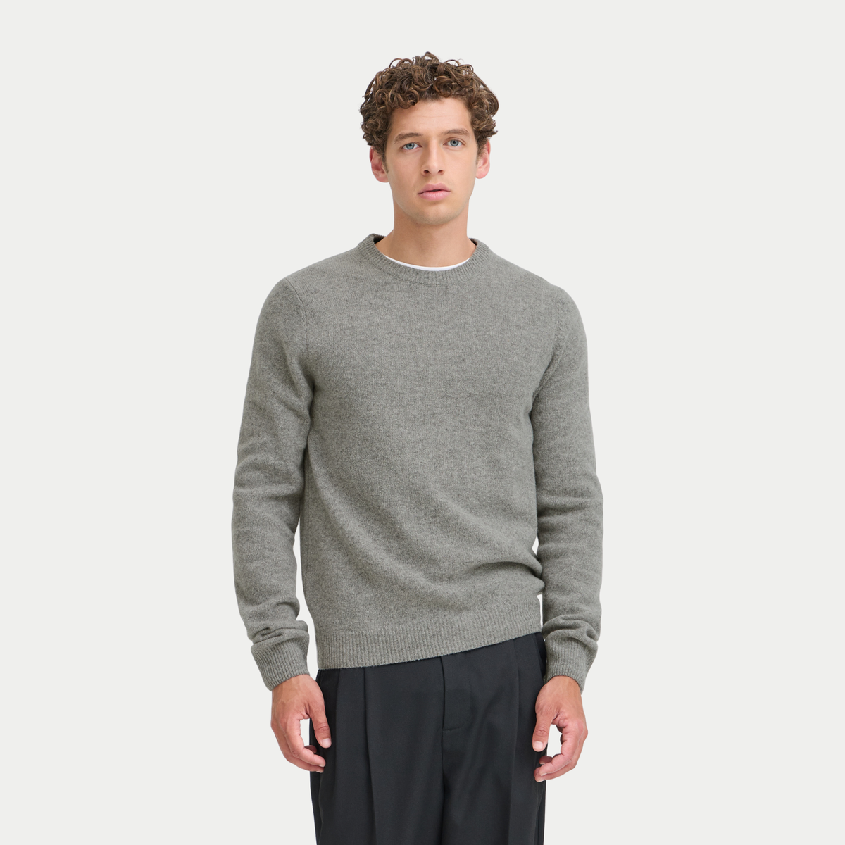 Pull gris chiné en laine d'agneau porté de face avec un pantalon noir, col rond bordé de côtes fines