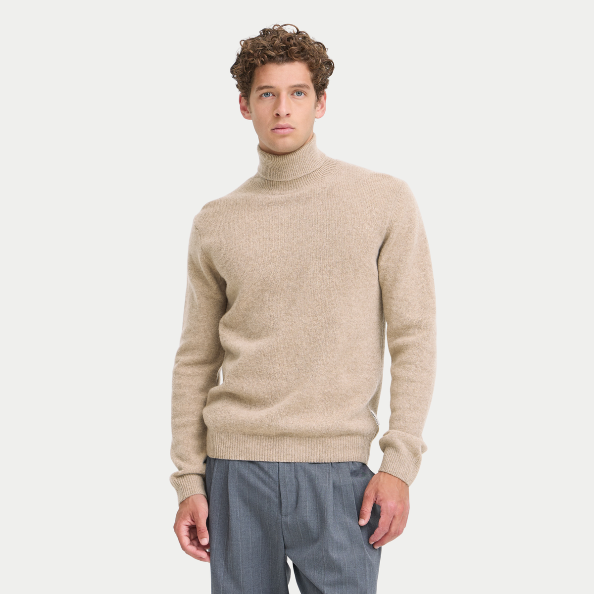 Col roulé beige sable porté de face, maille fine chinée et bas de corps côtelé, avec un pantalon gris