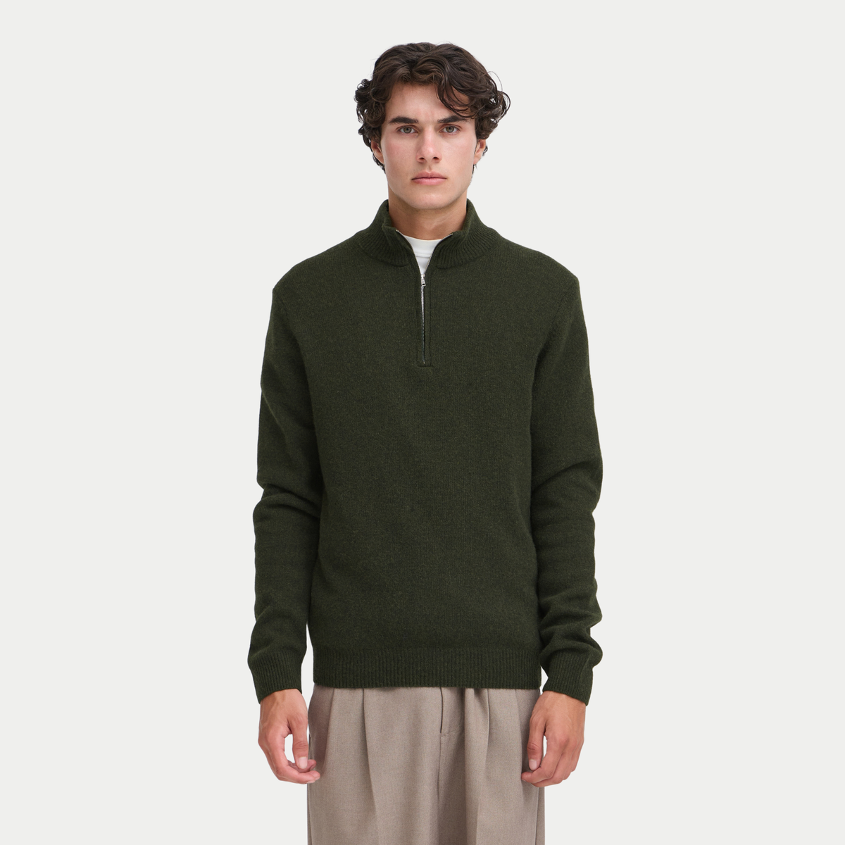 Pull half zip kaki porté de face sur un pantalon beige, zip argenté remonté au col