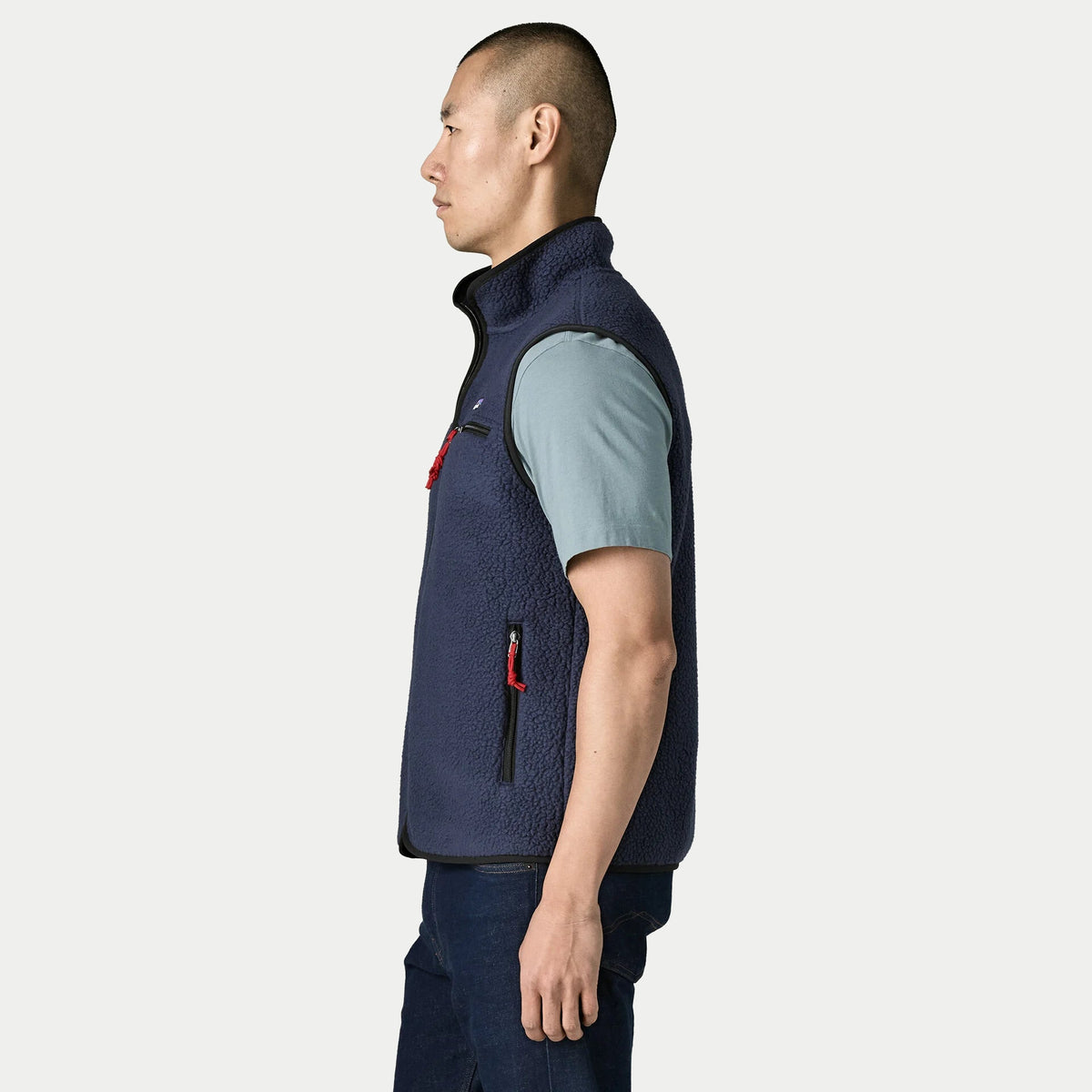 Gilet Retro Pile New Navy Patagonia de profil, emmanchure bordée de noir et poche basse zippée à tirette rouge