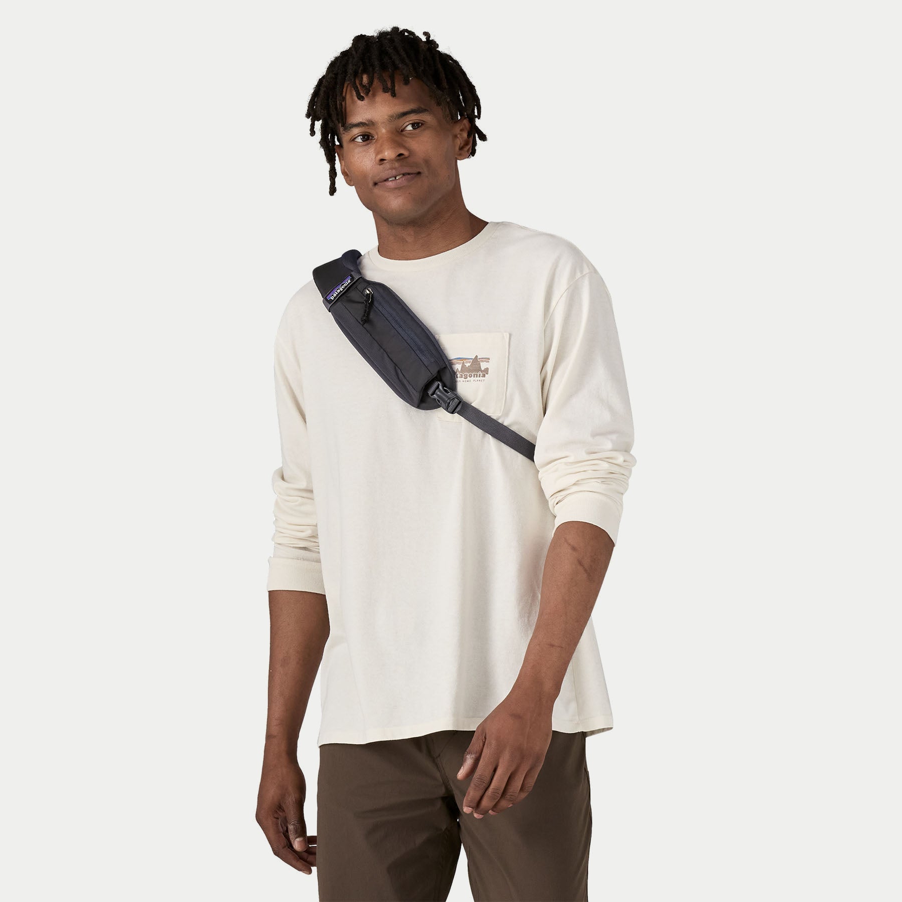 Atom Sling 8L Smolder Blue Patagonia porté devant sur le torse, poche zippée de la sangle et boucle clip