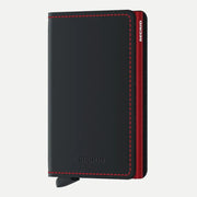 Portefeuille plat en cuir noir mat à surpiqûres rouges, boîtier rouge visible sur la tranche