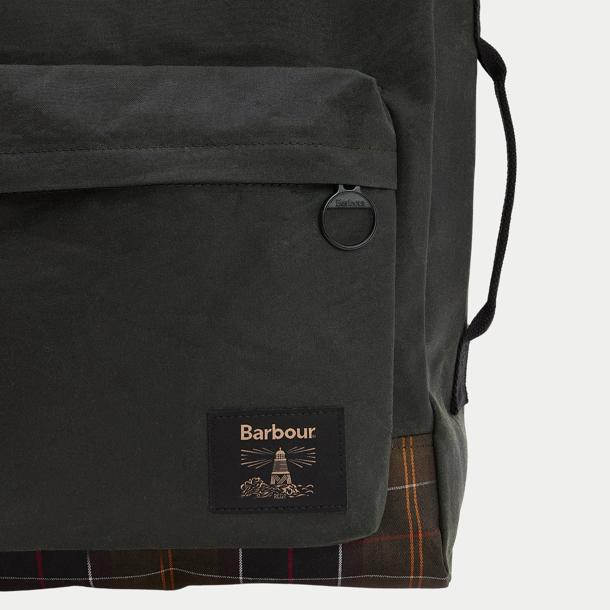 Détail de la poche avant zippée du sac à dos Field Wax Sage, patch Barbour et base en tartan Classic