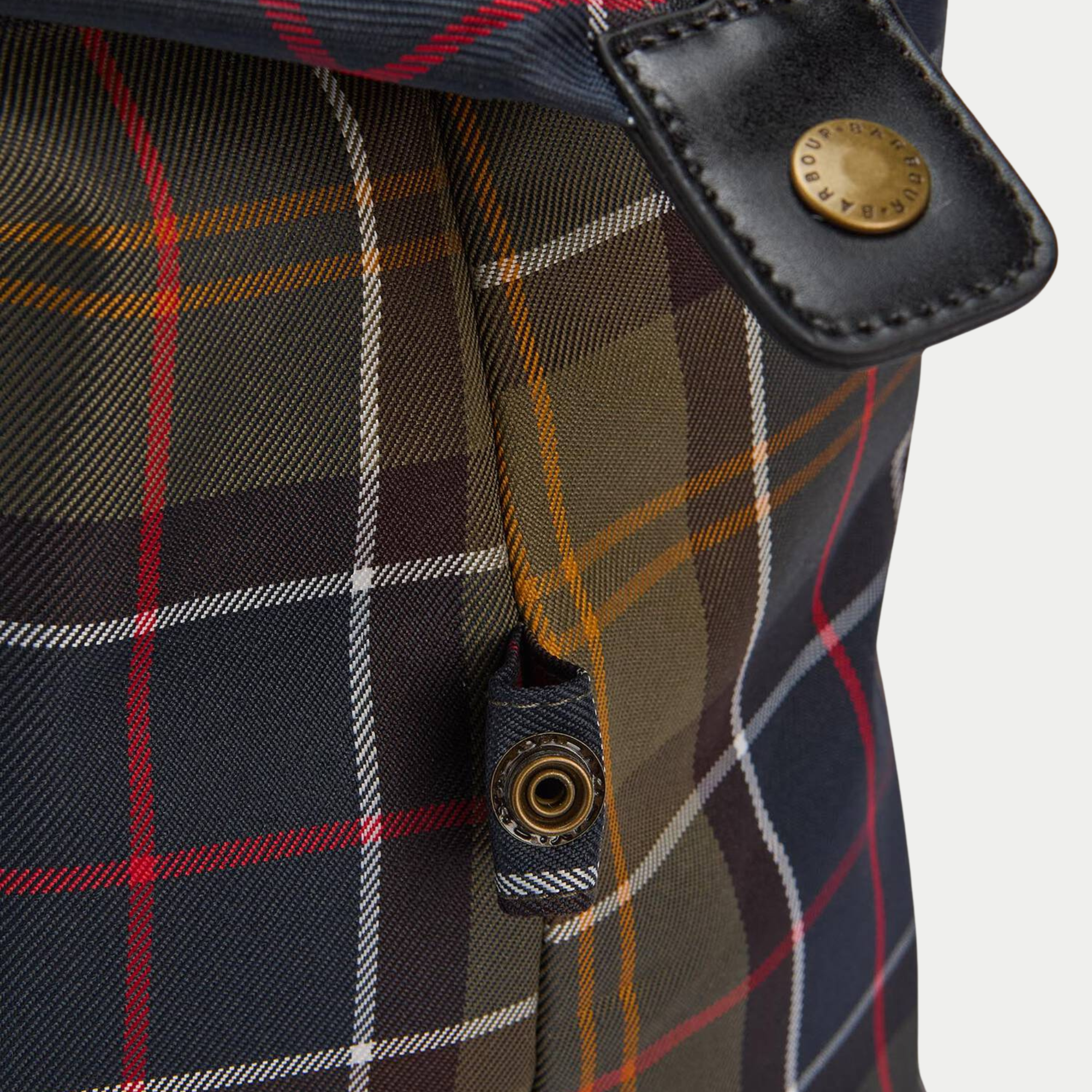 Détail du sac Torridon Barbour : patte en cuir noir et bouton pression laiton gravé Barbour