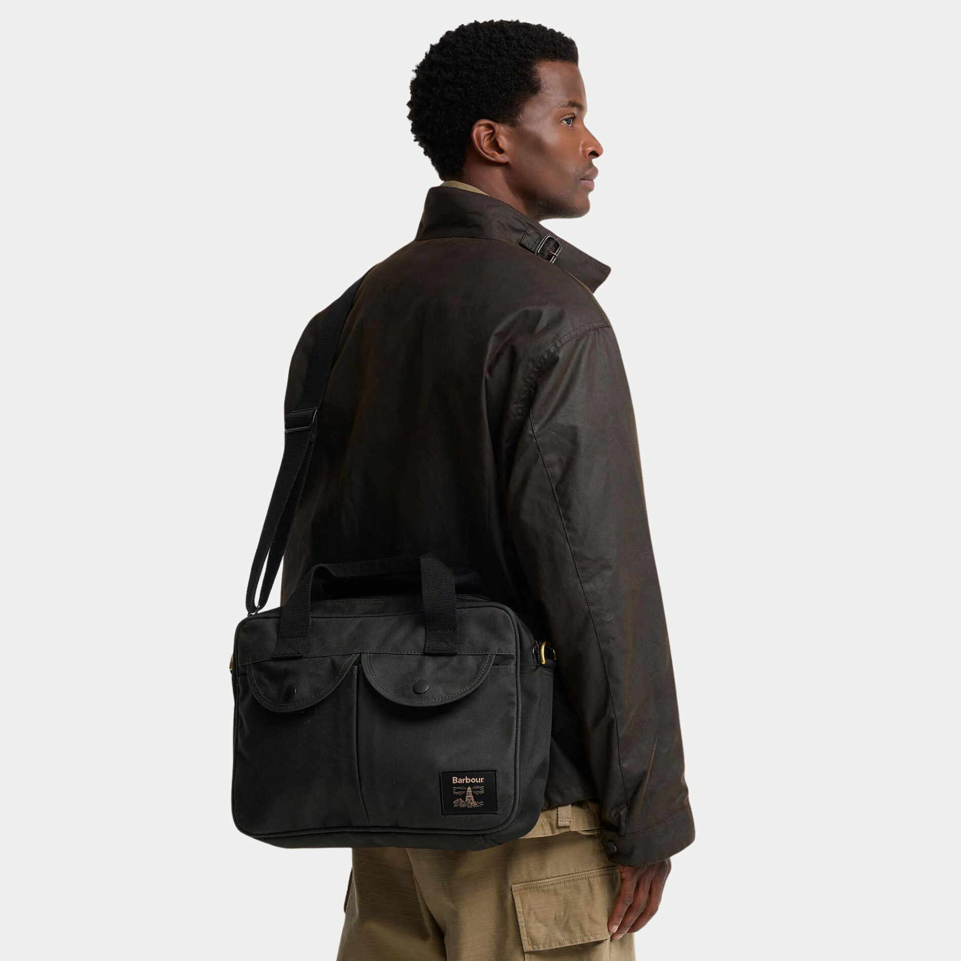 Sacoche ordinateur Barbour Wax Field Sage portée en bandoulière dans le dos avec une veste cirée