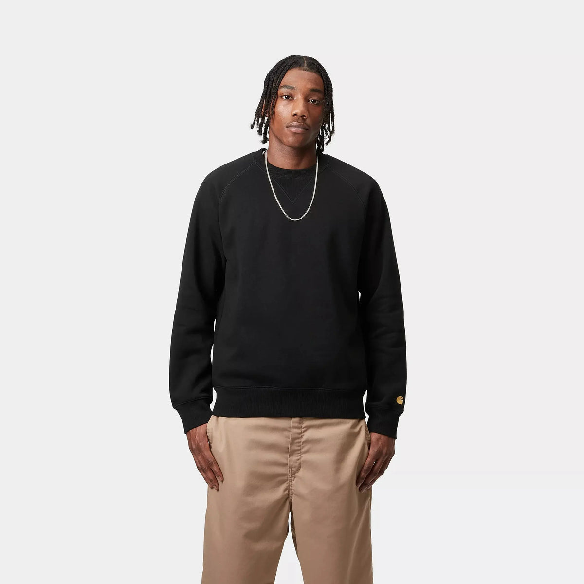 Sweat Chase Carhartt WIP noir porté de face sur un pantalon beige, encolure ronde côtelée et lignes raglan