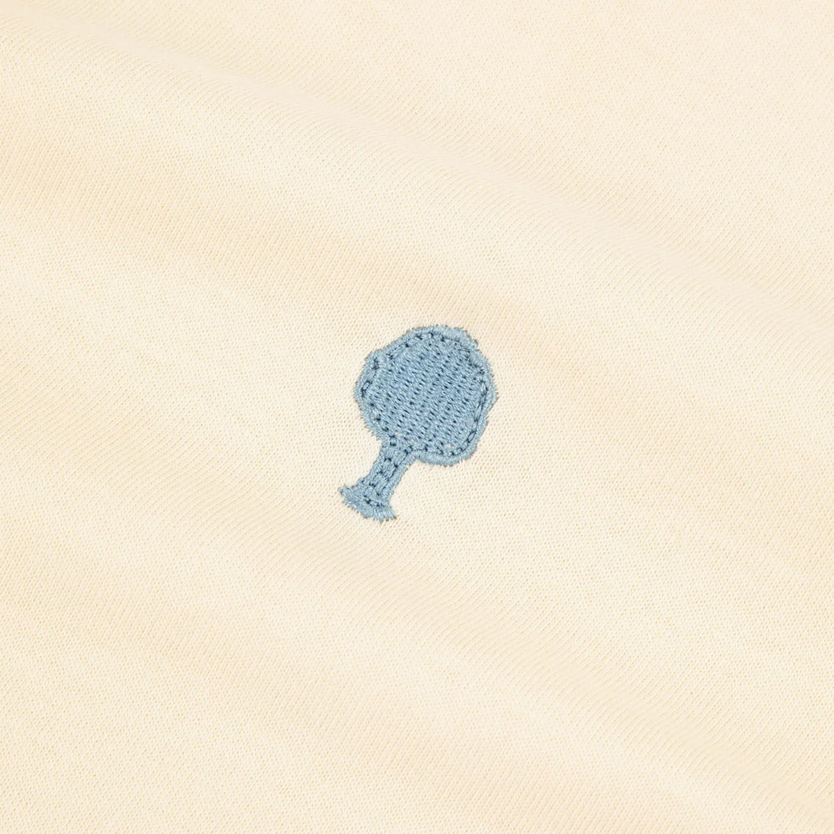Macro de l'arbre brodé bleu ciel sur le jersey de coton écru du T-shirt Arcy