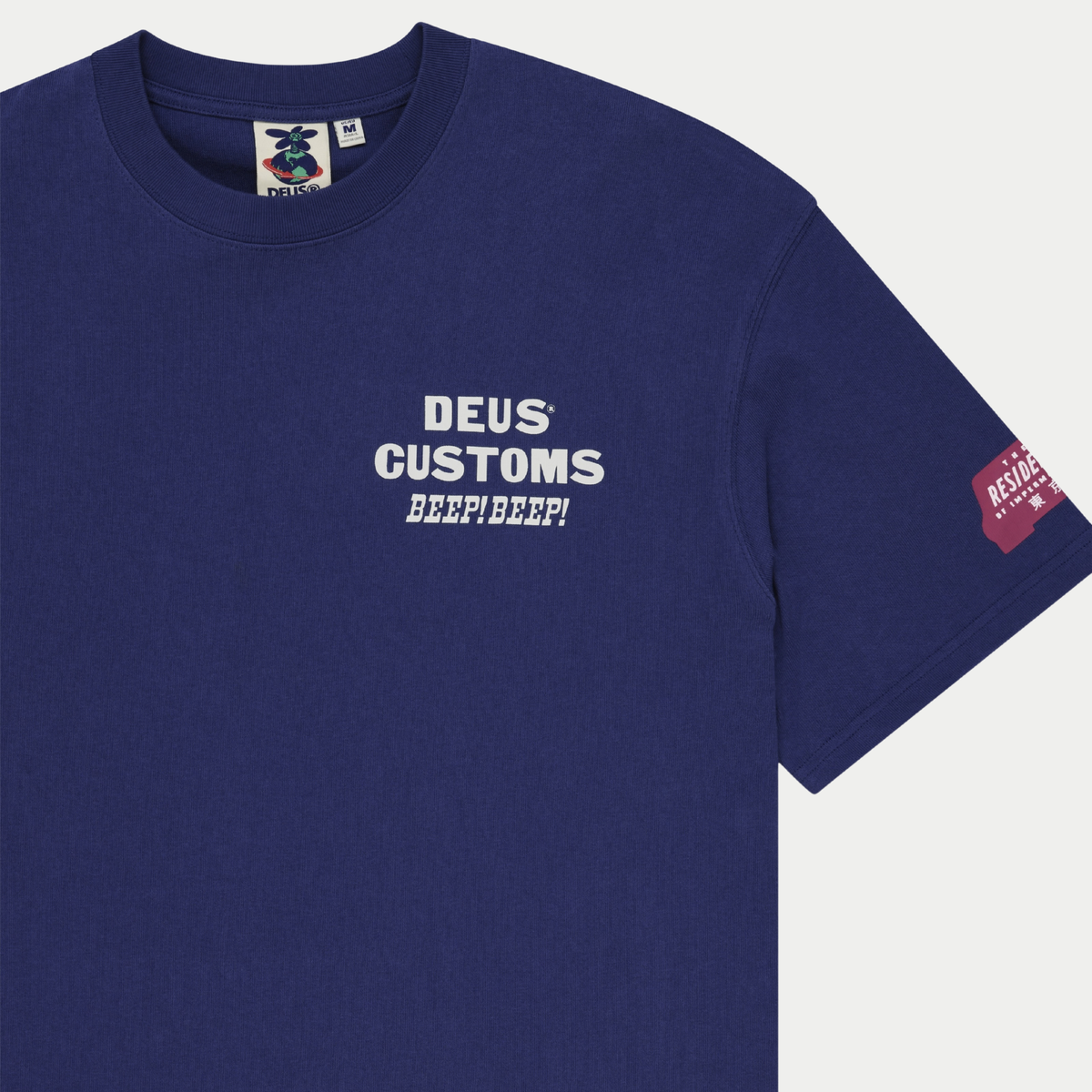 Gros plan poitrine du T-shirt Bloomers bleu marine : imprimé Deus Customs, étiquette de col et marquage framboise sur la manche