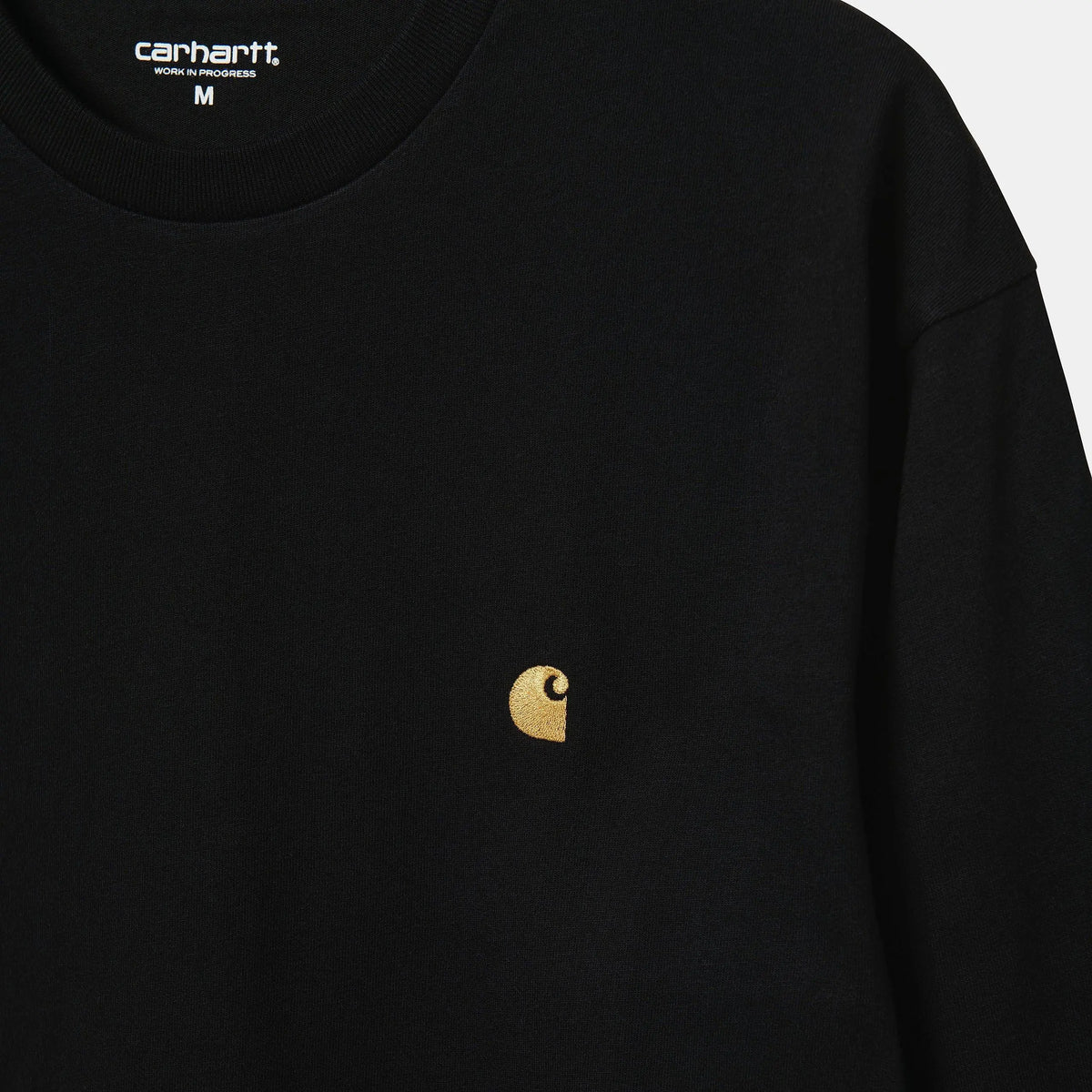 Gros plan du buste : étiquette Carhartt Work In Progress au col et broderie du logo C doré sur le jersey noir