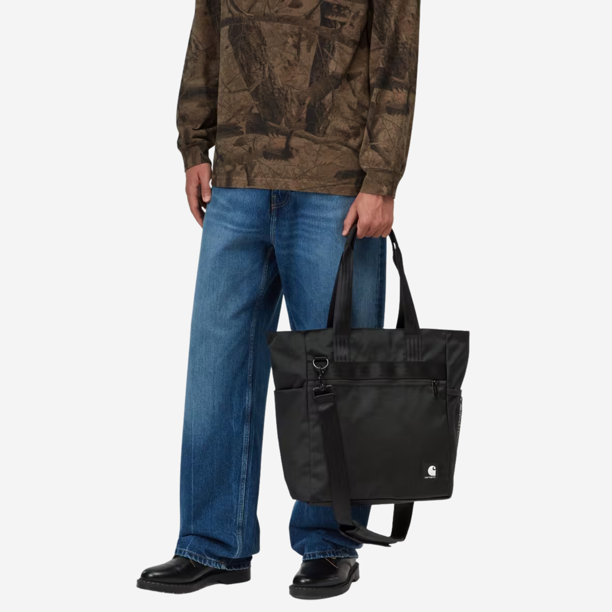 Tote bag Richmond noir Carhartt WIP porté à la main, hauteur de hanche, avec sa bandoulière détachée qui pend