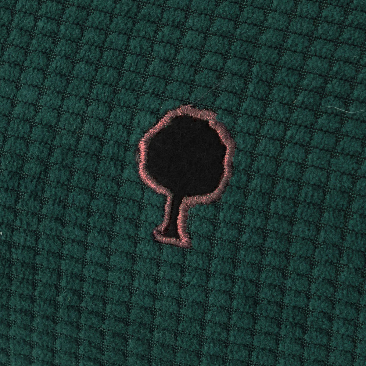 Gros plan sur le velours côtelé vert foncé de la trousse Faguo et son arbre brodé cerclé de rose