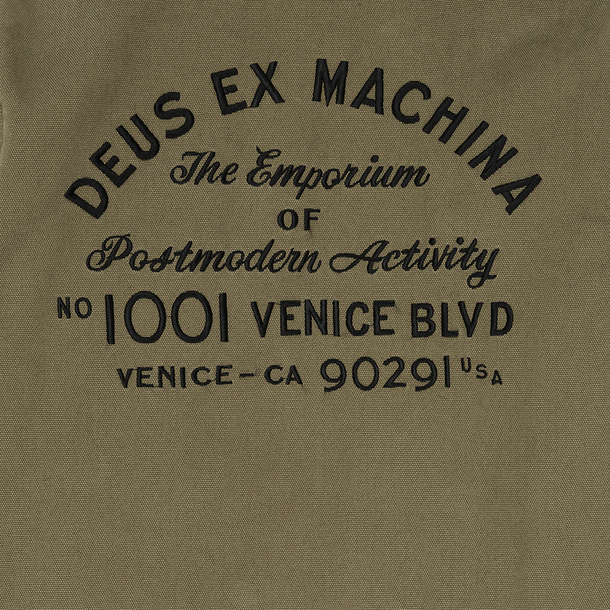 Gros plan de la broderie noire au dos de la veste Address Workwear Deus Ex Machina, toile de coton olive délavée
