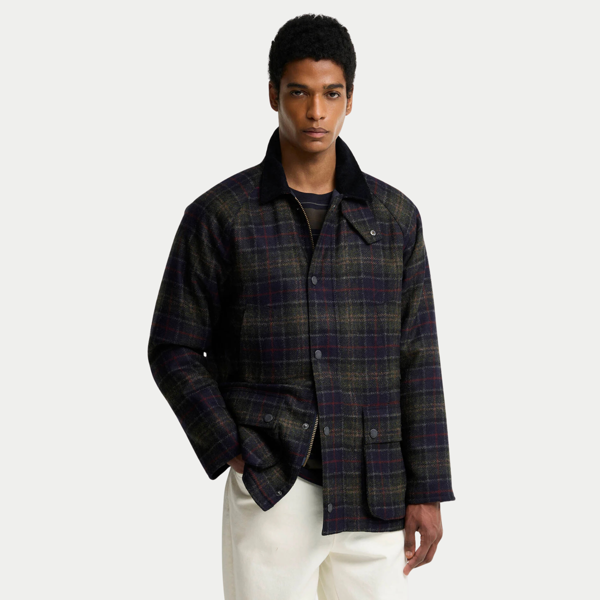 Bedale en laine tartan olive foncé portée ouverte sur un t-shirt rayé, une main en poche, manches raglan