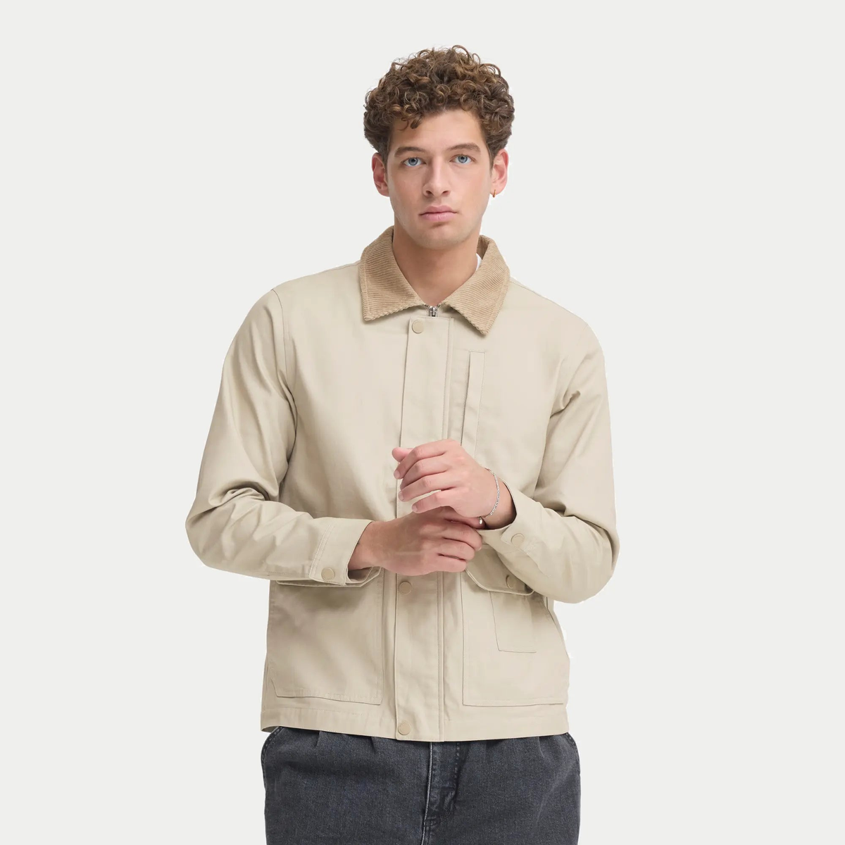 Veste en coton ciré beige portée ouverte sur un jean gris, zip et pressions ton sur ton