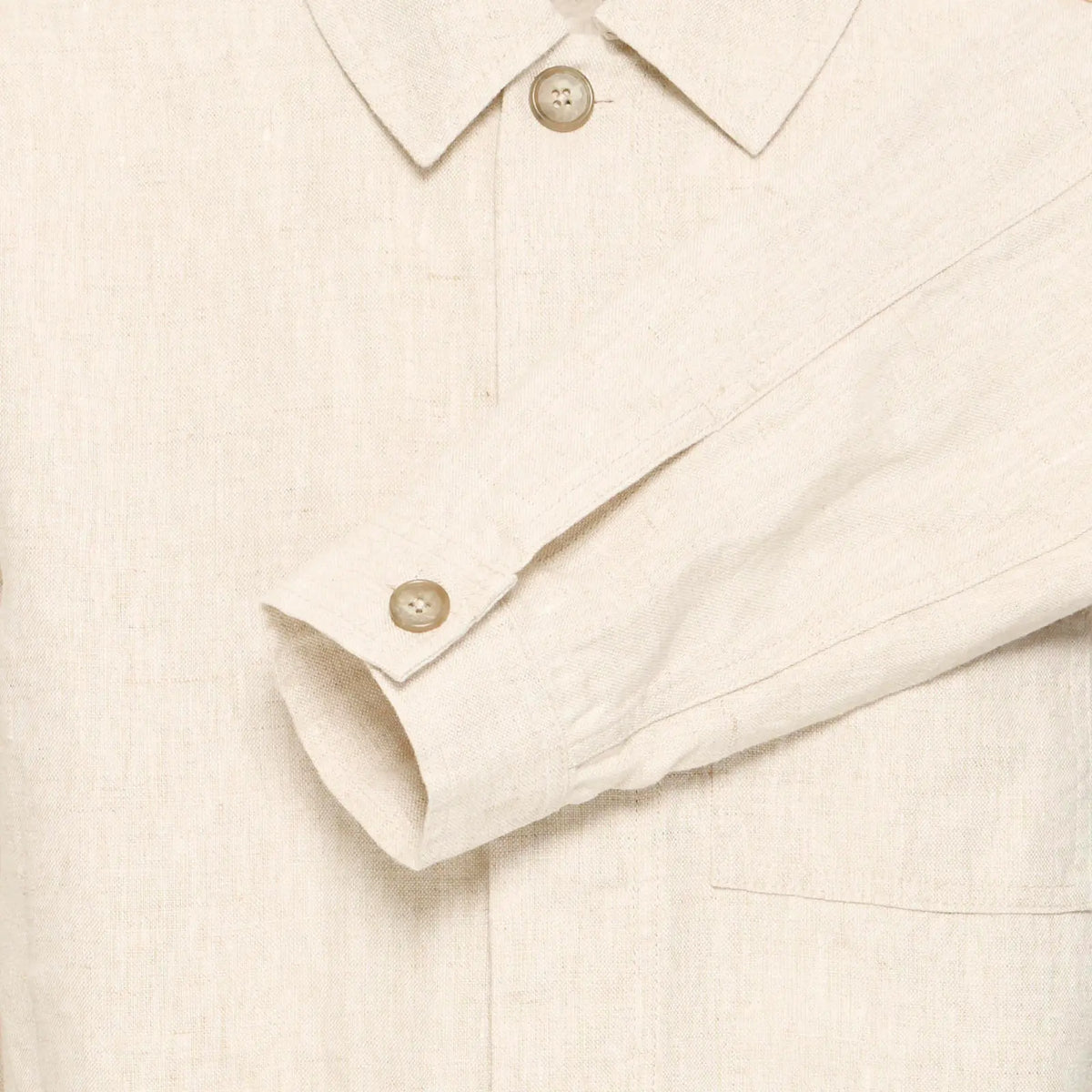 Gros plan sur le col, la patte de boutonnage et le poignet de la veste : boutons beiges et grain du lin