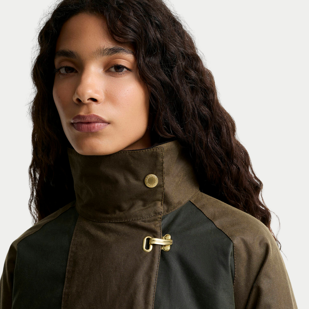 Gros plan du col montant de la veste Hazelwood en coton ciré olive, pression laiton gravée et crochet doré