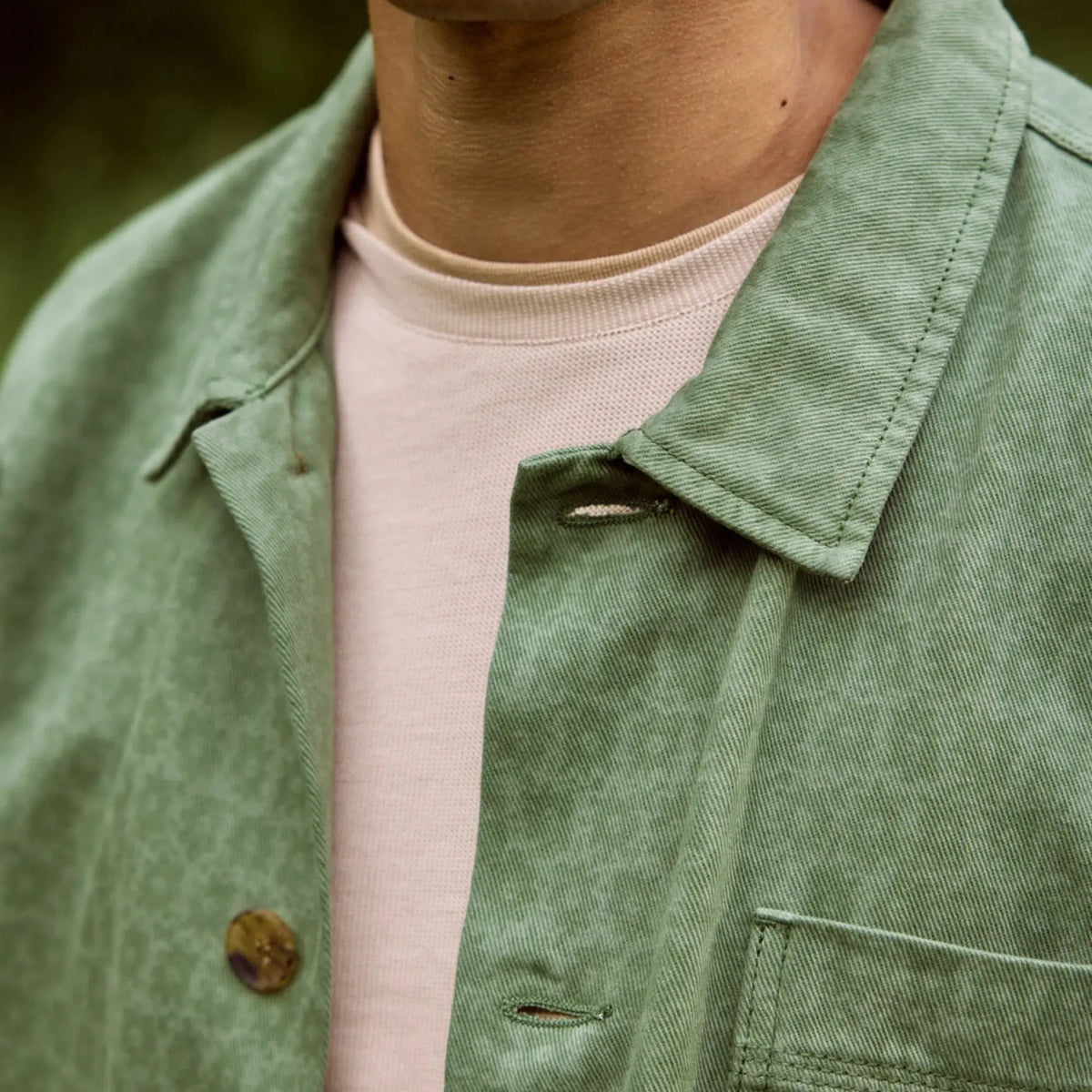Gros plan du col ouvert de la Lorge verte et de sa boutonnière sur un t-shirt rosé
