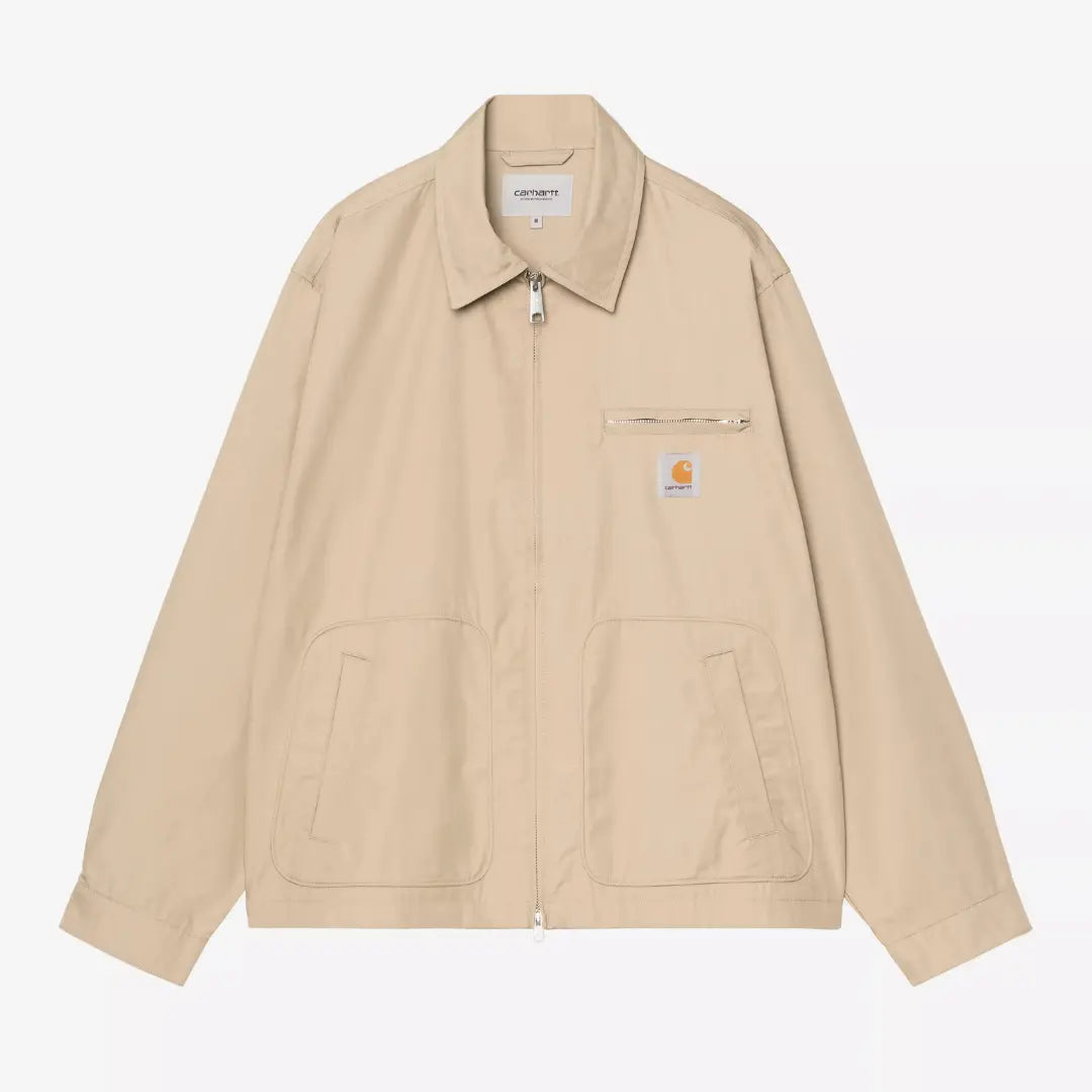 Veste Postal Iroko Carhartt WIP à plat : toile beige sable, col chemise, zip central, poche poitrine zippée